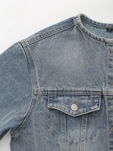 Detail of round neck and buttoned chest pocket on washed blue denim jacket with stitching