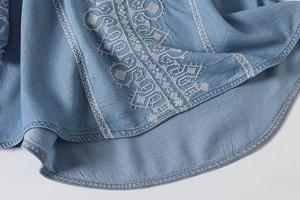 Close-up of white ethnic embroidery details on a light blue cotton summer blouse