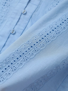 Detailed view of light blue shirt featuring intricate eyelet embroidery and buttons