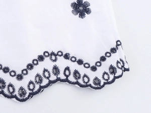 Détail de la broderie florale bleu marine et du bord festonné sur une chemise blanche