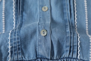 Detail of blue denim dress featuring pearlescent buttons and white floral embroidery