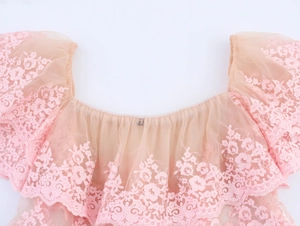 Detail of pink embroidered lace and layered mesh fabric on an off-shoulder top