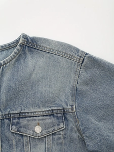 Close-up of washed blue denim jacket featuring raw edge collar and metal button pocket
