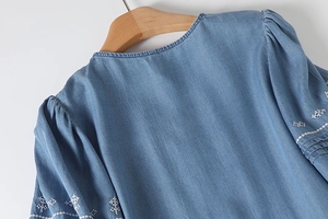 Detail of blue denim dress with white geometric embroidery on puff sleeves and gathered neck