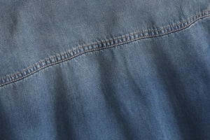 Detailed close-up showing double-needle stitching on blue denim fabric shirt