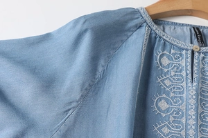 Detail of white ethnic embroidery and keyhole neckline on a light blue summer blouse