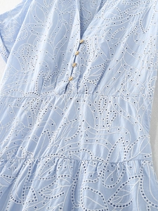 Detail van lichtblauwe broderie anglaise stof met V-hals en houten knopen