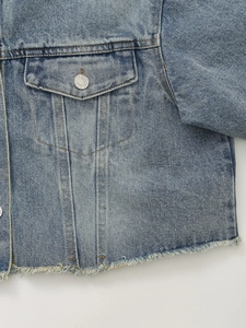 Detailed macro view of washed blue denim jacket featuring frayed hem and metal buttons