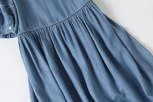 Detail of light blue denim dress featuring white floral embroidery and pleated waist design
