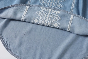 Detailed view of white geometric embroidery on light blue denim fabric with fine stitching
