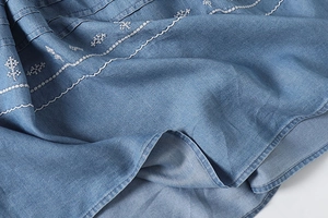 Detailed close-up of white floral embroidery on washed blue denim dress hemline