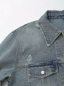 Detail of light blue washed denim jacket with distressed textures and metal buttons