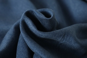 Macro shot of dark blue denim cotton fabric with dense twill texture and soft folds