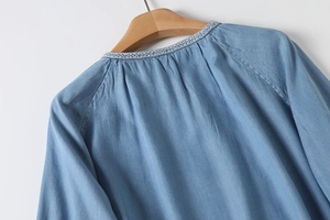 Detailed view of woven neckline embroidery and soft denim texture on a summer shirt