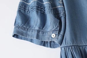 Detailed macro view of white embroidery and ruffled cuffs on this blue denim dress