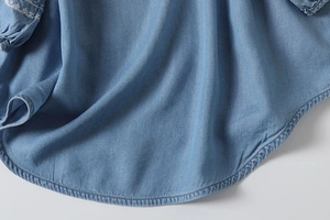 Detail of light blue denim shirt showing white ethnic embroidery and curved hemline