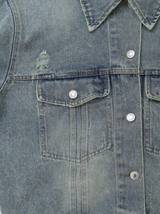 Detailed close-up of washed blue denim jacket featuring metal jeans buttons and distressed texture