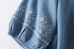 Close-up of white geometric embroidery on blue lantern sleeve of casual linen shirt