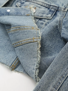 Detail of light blue denim jacket featuring raw hem edges and contrast double stitching