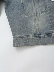Detail of washed blue denim jacket featuring stitching, metal button, and distressed texture