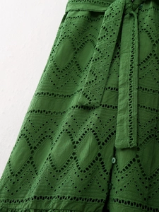 Close-up of dark green eyelet embroidery fabric with buttons and a matching waist belt