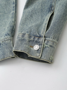 Light blue wash denim jacket cuff with vintage metal JEANS button and worn edge