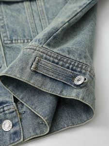 Close-up of vintage washed blue denim jacket with adjustable hem and metal buttons