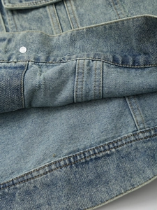 Detail of light blue denim jacket showing premium stitching and metallic rivets