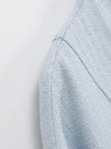 Macro shot of ice blue tweed jacket showing intricate metallic threading and shoulder seam
