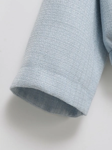 Close-up of light blue tweed jacket cuff showing premium woven texture and neat stitching
