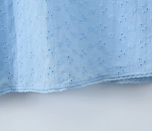 Detail of light blue eyelet embroidery fabric with floral patterns and woven lace trim