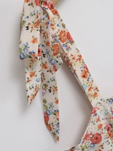 Detailed close-up of floral print on cream-colored dress with fine shoulder straps