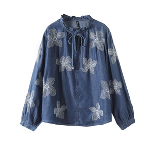 Détail de broderie florale sur chemise en denim bleu avec col à volants et lien