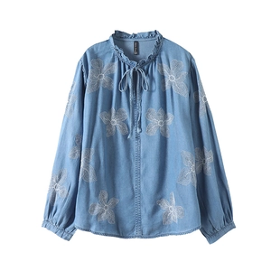 Détail de la broderie de fleurs blanches et du col à volants sur chemise en jean