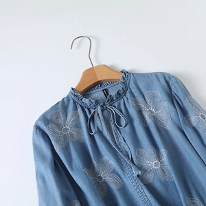 Détail de broderie florale blanche et col montant à volants sur chemise en jean bleu clair