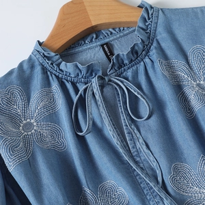 Détail d'une chemise en jean bleu clair avec col à volants et broderie florale