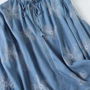 Détails de broderie florale sur chemise bleu denim avec col à volants et cordon