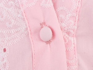 Detail of pink summer dress fabric with white hollow embroidery and fabric-covered button