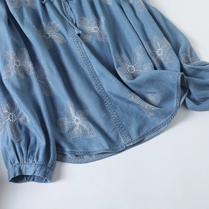 Détail de broderie florale blanche sur chemise en jean bleue avec encolure froncée chic