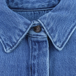 Gros plan du col de chemise en jean bleu avec texture sergée et bouton marron