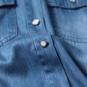 Macro shot of denim shirt fabric texture with high-quality white metal-edged button detailing