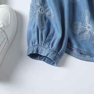 Détails de broderie florale sur manche de chemise en jean bleu clair avec poignet élastique