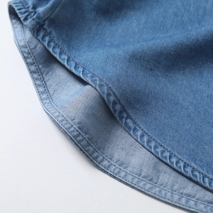 Macro detail of curved hem on blue tencel denim shirt with high-quality stitching