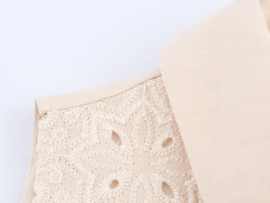 Detail of floral embroidery and eyelet texture on beige sleeveless dress fabric