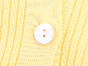 Detail of high-density ribbed knit texture in bright yellow with a pearlescent white button