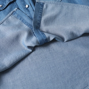 Detailed close-up of light blue tencel denim shirt with white pearl snap buttons
