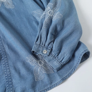 Détail de broderie florale blanche sur poignet de chemise en jean bleu avec bouton