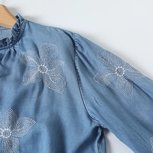 Détail de la broderie et du col à volants sur une chemise en jean bleu clair femme