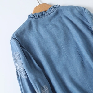Détail de broderie florale sur chemise denim bleu clair avec col volanté et cintre en bois