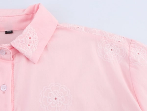 Détail de la broderie florale blanche sur le col et la texture de la chemise rose